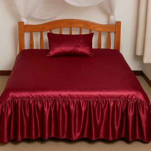 A neatly made double bed adorned with a rich burgundy satin bedcover, styled in a bright, cozy bedroom