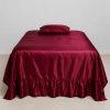 A deep burgundy satin bedspread with ruffled hem neatly laid on a full-sized bed