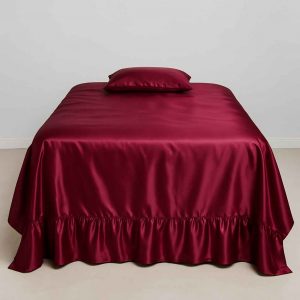 A deep burgundy satin bedspread with ruffled hem neatly laid on a full-sized bed