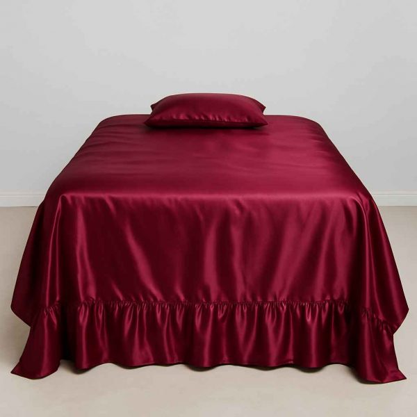 A deep burgundy satin bedspread with ruffled hem neatly laid on a full-sized bed