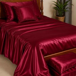 A photograph showcases a bedroom with a bed dressed in a luxurious satin bedcover set in deep burgundy