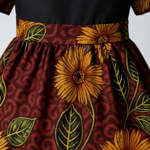 Close-up of a girls’ kitenge flare dress showing the waistline, pleats, and vibrant floral print on rich burgundy fabric