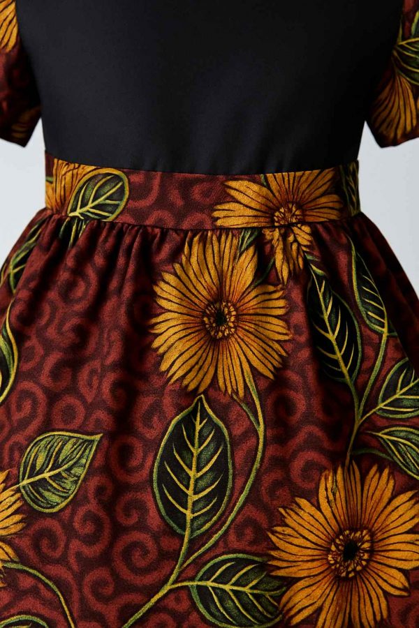 Close-up of a girls’ kitenge flare dress showing the waistline, pleats, and vibrant floral print on rich burgundy fabric