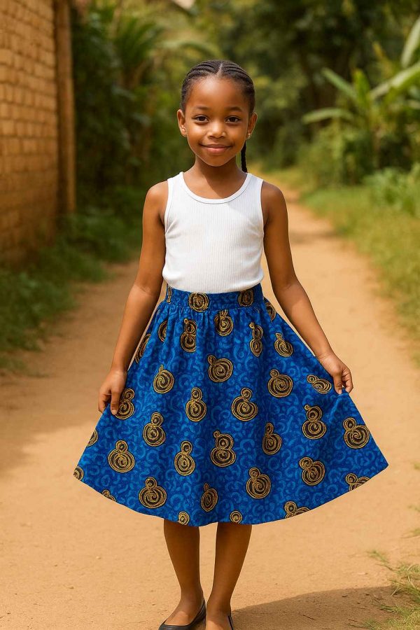 Young African girl wearing a bold Kitenge skirt in a natural outdoor setting, smiling softly and standing near a garden path.