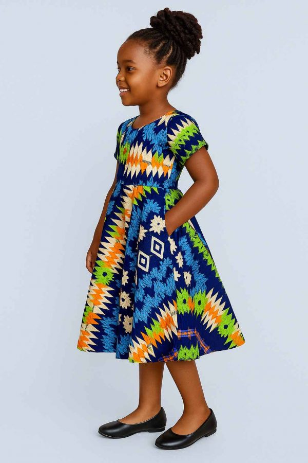 Young African girl in a multi-pattern kitenge flare dress smiling joyfully in side view