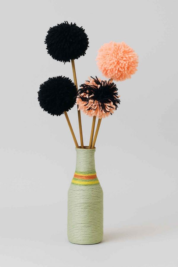 Studio image of a decorative yarn-wrapped bottle with a full arrangement of handcrafted pompom yarn flowers