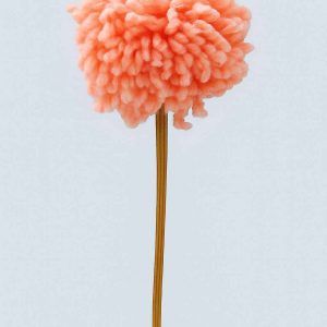 Studio image of a handcrafted peach yarn pompom flower on a wooden stem