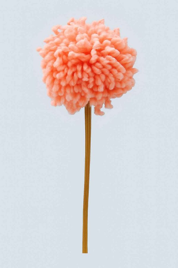Studio image of a handcrafted peach yarn pompom flower on a wooden stem