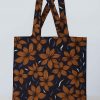 Front studio view of a handmade African print tote bag featuring orange floral design on dark background