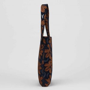 Side studio view of a handmade African print tote bag showing thin profile and double-stitched strap