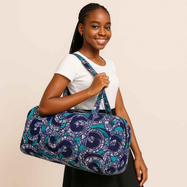 African woman confidently carrying a wax-print duffle bag in a clean studio setting