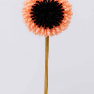 Studio photo of a handmade pompom flower with peach and black yarn on a wooden stem