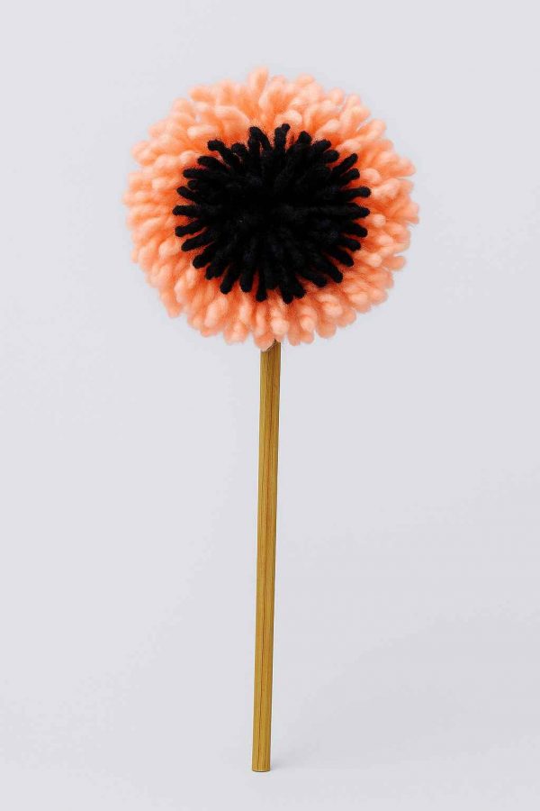Studio photo of a handmade pompom flower with peach and black yarn on a wooden stem