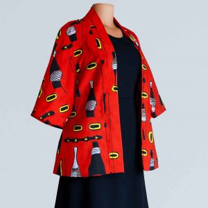 Angled view of a mannequin wearing a red African kitenge jacket with medium sleeves, styled over a dark skirt against a clean backdrop.