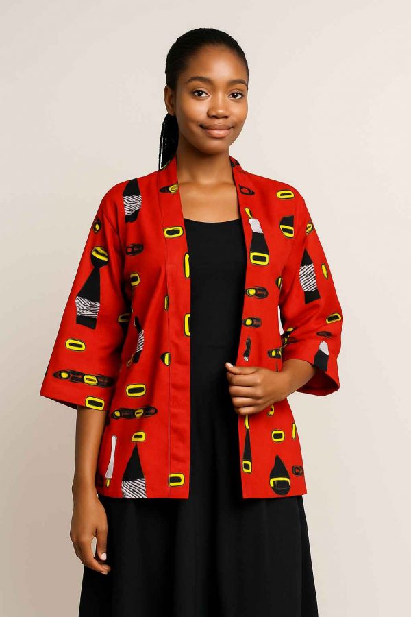 African woman modeling a red African kitenge jacket with medium sleeves and a dark skirt, standing gracefully in a clean studio setting.
