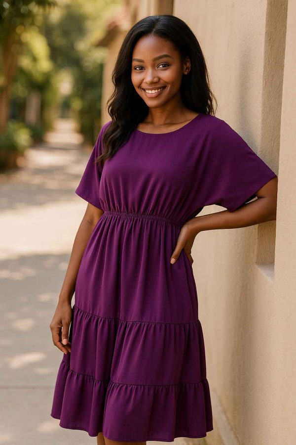 Young African woman in a royal purple modest midi dress standing gracefully in a sunlit outdoor walkway