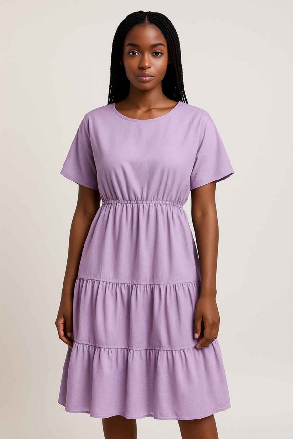 African seamstress showcasing a lavender tiered midi dress beside her sewing machine in a well-lit artisan workspace